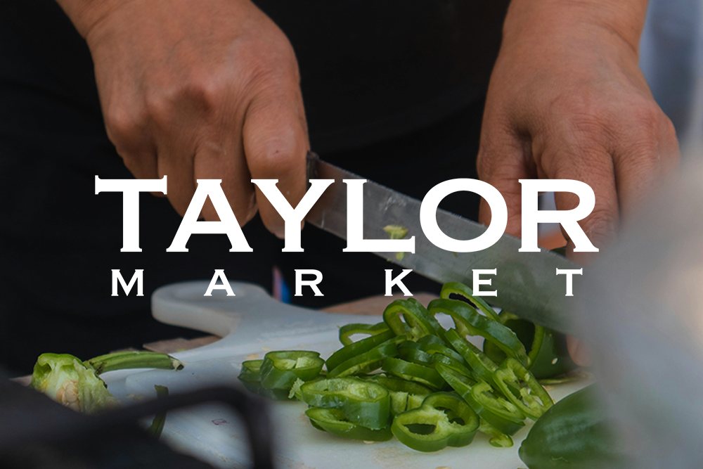 Un primer plano de hierbas siendo cortadas sobre una tabla de cortar y el logotipo de Taylor Market.